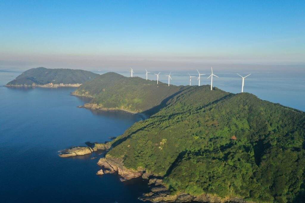 南東側から見た三崎ウインドパークの風車群（写真奥には、佐田岬半島最西端の伊方町正野地区にある漁港が確認できる）