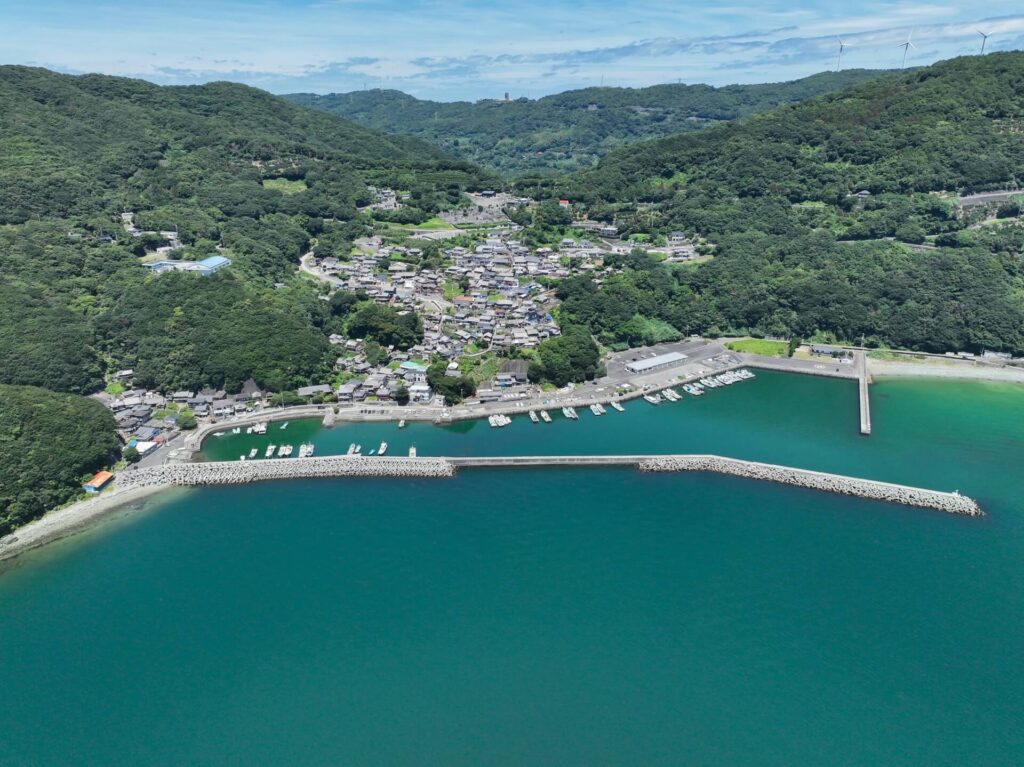 伊方町の豊之浦漁港と、伊方ウィンドファームの風車（写真右上が、伊方ウィンドファームの風車）